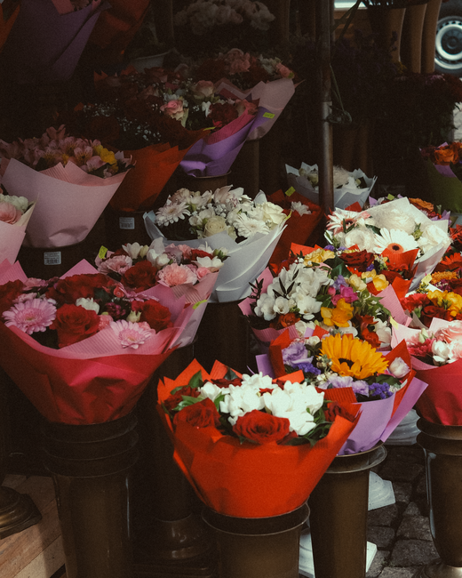 A display of various flower bouquets arranged on black cylindrical stands, featuring a diverse assortment of fresh flowers including roses, daisies, and other mixed blooms in vibrant reds, whites, pin